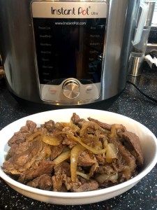 a white bowl filled with beef and onions next to an instant pot