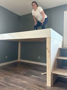 a woman standing on top of a white loft bed in a room with hardwood floors