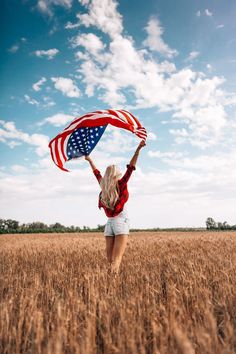 a woman standing in a field holding an american flag over her head and looking at the sky