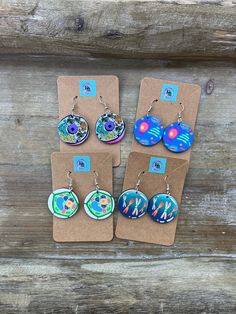 four pairs of earrings are displayed in front of a piece of cardboard on a wooden surface