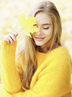 a beautiful young blond woman holding a leaf in her hand and smiling at the camera