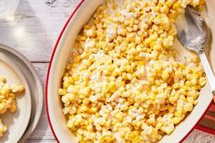 a bowl filled with corn on top of a table next to two plates and spoons