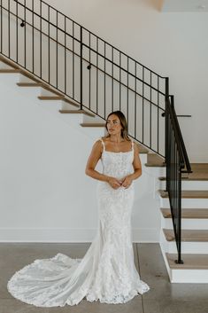 a woman standing in front of a staircase wearing a wedding dress and looking at the camera