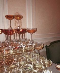 a table topped with lots of wine glasses next to a black chair and white wall