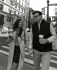 a man and woman are walking down the street holding coffee cups in their hands while looking at each other