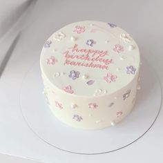 a white cake with pink and purple flowers on it's side sitting on a plate