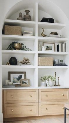 a white bookcase with wooden drawers and shelves filled with books, vases and other items