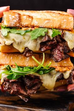 a hand holding a sandwich with meat, cheese and lettuce on it in front of a black background