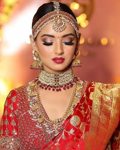 a woman in a red and gold bridal outfit with jewelry on her head, looking down