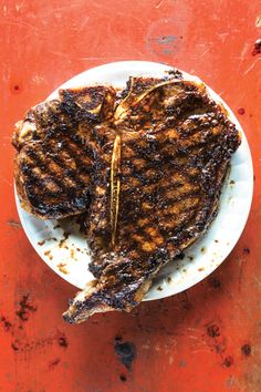 grilled meat on a white plate sitting on an orange table