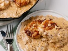 a white plate topped with chicken covered in gravy next to a skillet