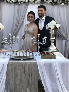 a man and woman standing next to each other near a table with silverware on it