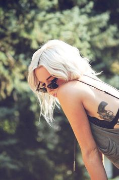 a woman with white hair and tattoos on her back looking down at something in the ground