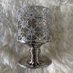 a silver candle holder with snowflakes on the top and bottom, sitting on a white furnishing