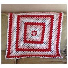 a red and white crocheted blanket sitting on top of a couch next to a pillow