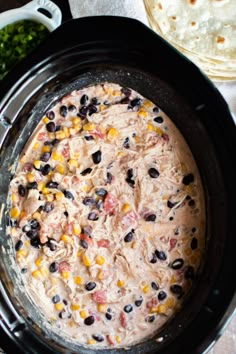 a crock pot filled with black beans and corn next to tortilla shells