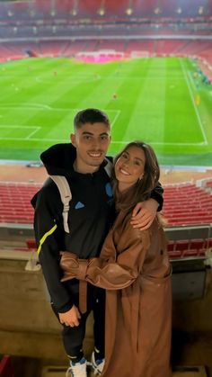 a man and woman standing in front of an empty soccer stadium with the lights on