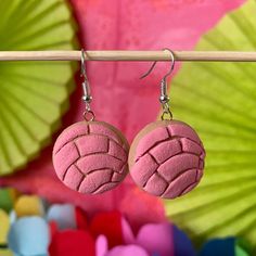 two pink earrings are hanging from a wooden stick in front of some colorful paper leaves