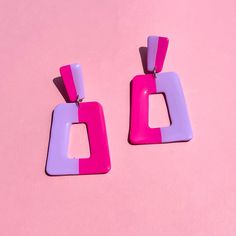 two pairs of pink and purple square shaped earrings on a pink background with copy space