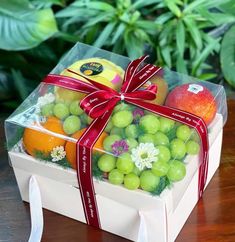 a clear box filled with assorted fruit on top of a wooden table next to green plants