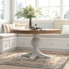 a white table and bench in a room next to two windows with pillows on them