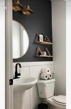 a white toilet sitting next to a bathroom sink under a mirror and gold accents on the wall