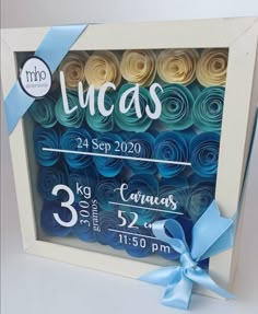 a photo frame with rolled paper flowers in blue, yellow and white colors that say lucas