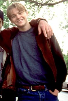 two young men standing next to each other in front of a tree with their arms around one another