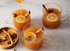 three mugs filled with orange juice and cinnamon garnish on top of a table