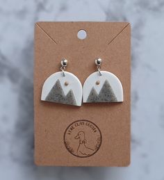 pair of white and grey earrings with mountains on them sitting on top of a card