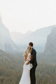 a bride and groom standing on top of a mountain