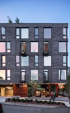 an apartment building with lots of windows and people walking on the sidewalk