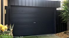 a black garage door in front of a house with yellow flowers on the side walk