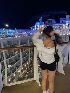 a woman standing on top of a balcony next to a cruise ship at night with her hair blowing in the wind