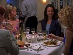 people sitting at a table with wine glasses and plates of food in front of them