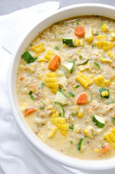 a white bowl filled with corn, carrots and zucchini soup on top of a white napkin