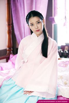 a woman sitting on top of a bed in a pink dress