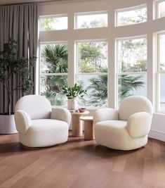 two white chairs sitting in front of large windows next to a table with a potted plant on it