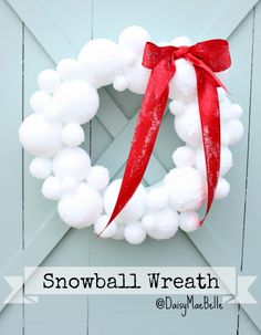 a snowball wreath hanging on the side of a door with a red ribbon around it