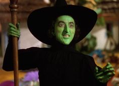 a man dressed as the wizard holding a broom and wearing green makeup on his face