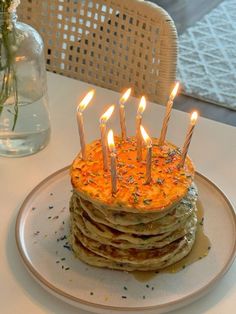 a stack of pancakes sitting on top of a white plate with candles sticking out of them