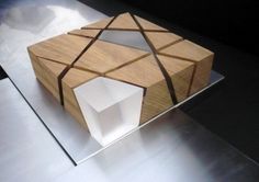 an unusual wooden object is sitting on the floor in front of a glass box with a ribbon around it