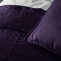 a bed with purple sheets and pillows on it