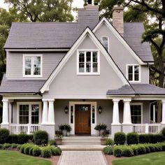 a gray house with white trim and two front porches on the first floor is surrounded by greenery