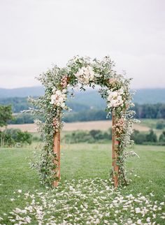 an outdoor wedding ceremony with flowers and greenery on the arch, surrounded by lush green grass