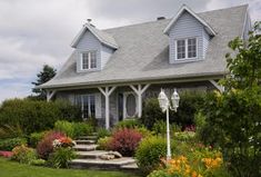 a house that is sitting in the grass with flowers around it and steps leading up to the front door