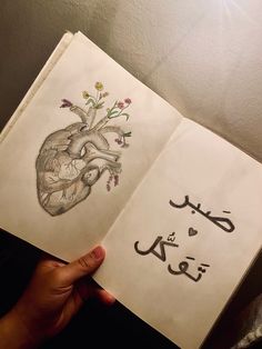 someone is holding an open book with arabic writing on it and a drawing of a human heart