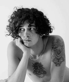 a shirtless man with long curly hair and tattoos on his chest is posing for the camera