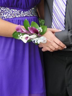 a man in a suit and tie holding a bouquet of flowers next to a woman in a purple dress