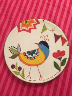 a plate with a colorful bird painted on it's side sitting on a red and white striped table cloth